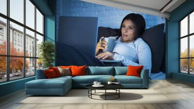 young beautiful hispanic woman on bed at home working happy on laptop computer at night Wall mural