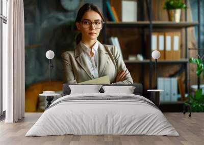 Confident and Composed: A professional woman in a beige suit and glasses stands confidently with her arms crossed, exuding an air of competence and determination.  She's in a stylish and modern office Wall mural