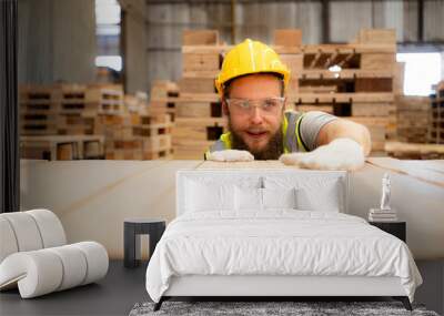 A guy carpenter in a hardhat and glasses inspects a completed work item at a timber industry. Wall mural