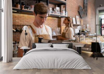 Barista working in cafe. Portrait of young male barista standing behind counter in coffee shop. Wall mural