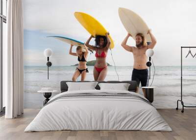 Rear view of two women and young man holding surfboards on their heads and walk into the sea to surf Wall mural