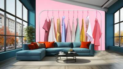 Collection of pastel colored women clothes hanging on rack in dressing room isolated on pink background Wall mural