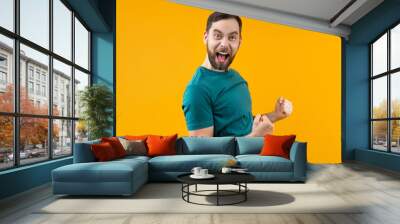 Portrait of joyful young man with wide open mouth and clenched fists celebrating money win in online lottery or at bookmaker's, isolated over yellow background Wall mural