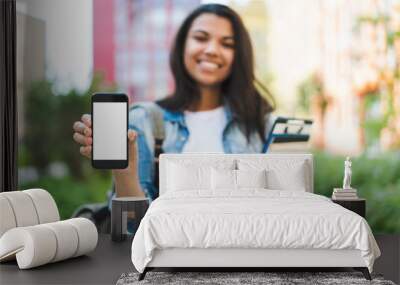 Smiling african american girl student holding smartphone in hands demonstrating its white blank screen to the camera. Focus is on hand with phone. Mock up, copy space for your text or interface Wall mural