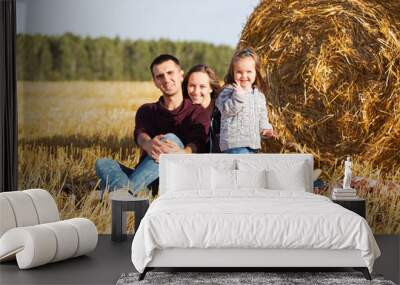 Happy young family with 2 year old girl next to hay bales in harvested field Wall mural