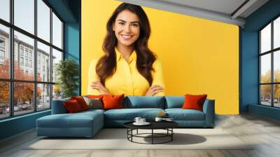 Confident young woman standing with her arms crossed on yellow background Wall mural