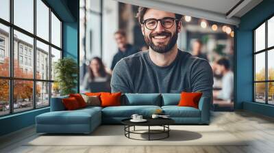 Portrait of a business man sitting in an office with his colleagues in the background. Happy business man working in a co-working office. Wall mural