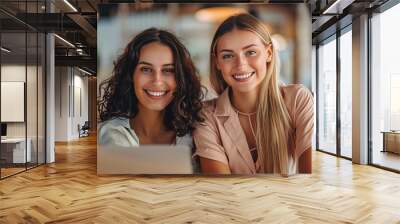 Two Women Smiling Together: A portrait of two young women, radiating happiness and warmth as they work together on a laptop in a modern cafe setting.  Wall mural