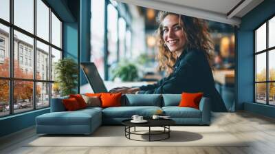 Young happy business woman company employee sitting at desk working on laptop. Smiling female professional entrepreneur worker using computer in corporate modern office looking at camera Wall mural