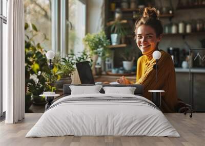 Young smiling pretty business woman student sitting at table at home office with laptop computer looking at camera advertising elearning online course Wall mural