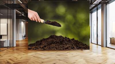 Hand pouring black soil with shovel on green bokeh background. Planting a small plant on a pile of soil or pouring soil during funeral. Gardening backdrop for advertising. Wall mural