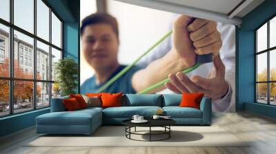 Close up hand patient doing stretching exercise with a flexible exercise band and a physical therapist hand to help in clinic room. Wall mural