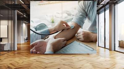 Doctor using stethoscope take a tap on the patient's arm and pressing pressure gauge button. Wall mural