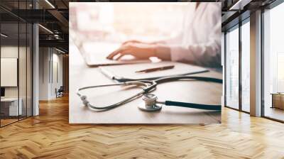 Stethoscope and background doctor using laptop at desk in clinic working on computer at room office. Wall mural