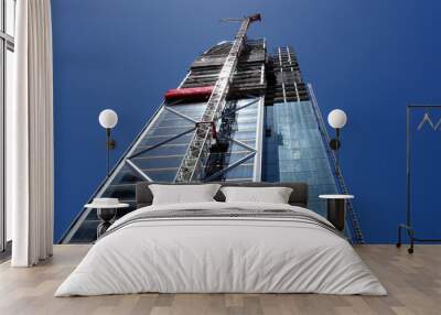 A tall skyscraper beeing built in Newzealands largest city Auckland. Looking at the modern facade made out of glass and steel with a large construction crane on it Wall mural