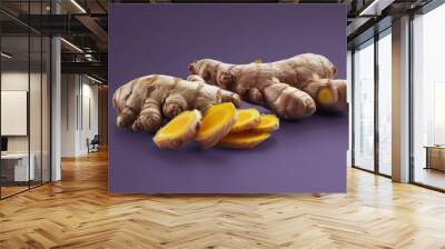 A minimalist, modern still-life photograph showing ginger and turmeric roots, along with sliced sections, arranged together in a cohesive and balanced composition on a deep purple background  Wall mural