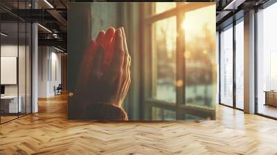 A vintage photograph of a person's hands clasped in prayer, with sunlight streaming through a window Wall mural