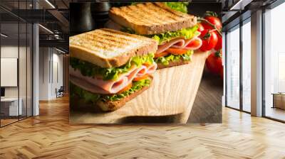 Close-up of two sandwiches with bacon, salami, prosciutto and fresh vegetables on rustic wooden cutting board. Club sandwich concept. Wall mural