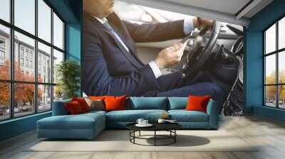 a businessman driving a prestigious car holds a mobile phone in his hand. Hasty life Wall mural