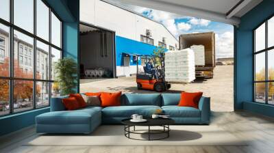 A man on a forklift works in a large warehouse, unloads bags of raw materials into a truck for transportation Wall mural