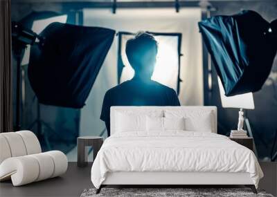 A man stands in front of a lighted backdrop with a black backdrop behind him Wall mural