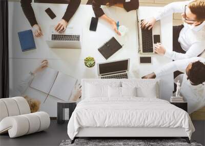 A team of young businessmen sitting at the table, top view, working and communicating together in an office. Corporate businessteam and manager in a meeting. Wall mural