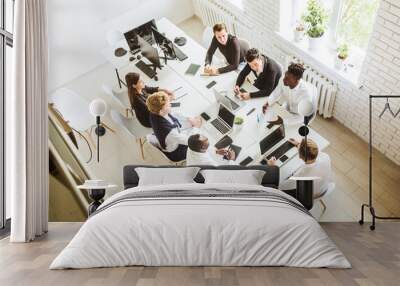 A team of young businessmen sitting at the table, top view, working and communicating together in an office. Corporate businessteam and manager in a meeting. Wall mural