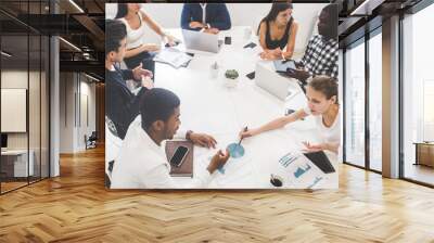 A team of young office workers, businessmen with laptop working at the table, communicating together in an office. Corporate businessteam and manager in a meeting. coworking. Wall mural