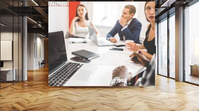 A team of young office workers, businessmen with laptop working at the table, communicating together in an office. Corporate businessteam and manager in a meeting. coworking. Wall mural