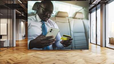 African American businessman makes online purchases from the phone while sitting in the back seat of the car and using a credit card Wall mural