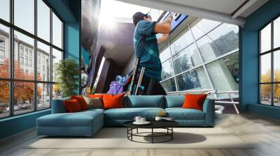 An employee of a professional cleaning service in overalls washes the facade and windows with special devices Wall mural