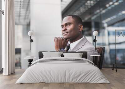 black man businessman in a business suit, expensive watch and glasses sitting on a bench against the backdrop of a modern city Wall mural