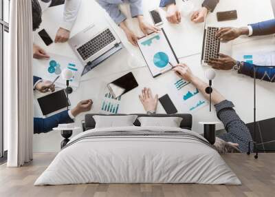 Documents, gadgets and hands of people on the desktop, top view. A team of young businessmen working and communicating together in an office. Corporate businessteam and manager in a meeting. Wall mural