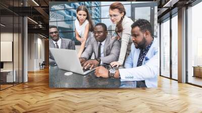 Group of happy diverse male and female business people team in formal gathered around laptop computer in bright office against the background of a glass building Wall mural