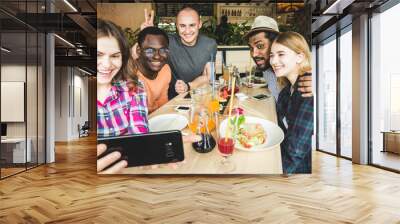 Group of young cheerful friends are sitting in a cafe, eating, drinking drinks. Friends take selfies and take pictures. Wall mural