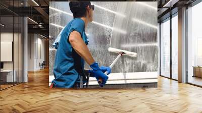 Male professional cleaning service worker in overalls cleans the windows and shop windows of a store with special equipment Wall mural