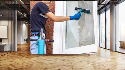 Male professional cleaning service worker in overalls cleans the windows and shop windows of a store with special equipment Wall mural