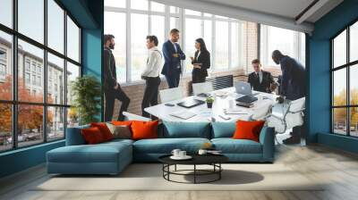 Mature businessman to discuss information with a younger colleague. People working and communicating while sitting at the office desk together with colleagues sitting. Wall mural