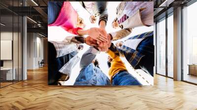 Bottom view of united young group of diverse people standing in circle joining hands showing support and cooperation. Youth community and teamwork concept with student friends stacking hands. Wall mural