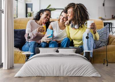 Cheerful multiracial female friends enjoying free time together at home - Three happy young adult women hanging out while - Friendship and social gathering concept Wall mural