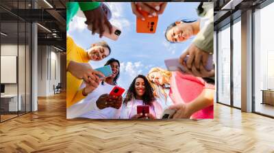 EvotoLow angle view of young group of multicultural women using mobile phones. Millennial females chatting on smart phone at city street. Blue sky. Wall mural