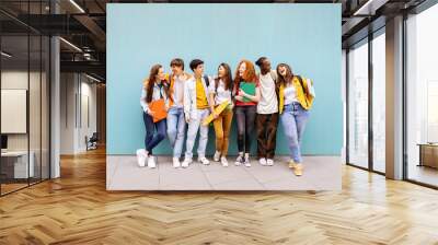 Happy multiracial students standing over isolated blue background. Diverse teenage friends having fun talking leaning on campus building college wall Wall mural