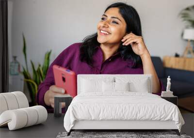 Happy relaxed young indian woman using cell phone while relaxing at home. Technology lifestyle concept. Wall mural