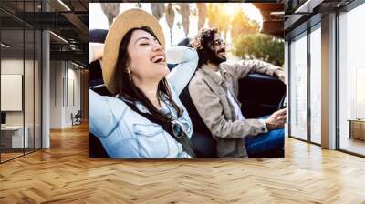 Happy young couple laughing together while driving a convertible car on holidays - Two millennial people having fun during road trip on summer vacation - Travel and rental auto service concept Wall mural