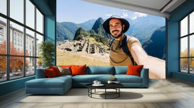 Happy young traveler man taking selfie portrait while enjoying vacation in Peru. Joyful tourist visiting Machu Picchu. Travel and holiday lifestyle concept. Wall mural