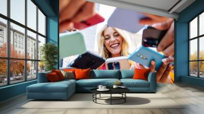 Low angle view of happy millennial people using smart phone devices together at city street. Technology lifestyle and social media concept. Wall mural