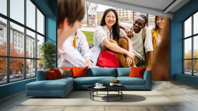 Multi-ethnic high school student friends sitting outdoors at campus park. Millennial college people having fun social gathering outside. Education and youth concept. Wall mural