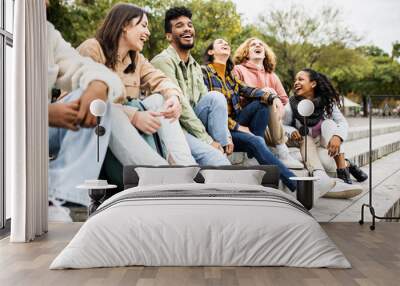 Multiracial group of young teenage student friends laughing together and having fun sitting on city street - United diverse millennial people celebrating together outside - Unity and community concept Wall mural