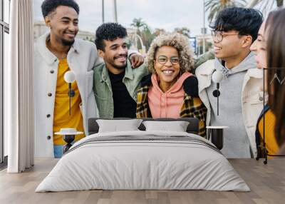 Multiracial young friends having fun in city street. United millennial people hugging each other standing together outdoors. Multi-ethnic friendship and youth concept Wall mural