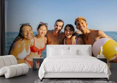 Portrait of diverse friends looking at camera hugging each other at beach during summer vacation Wall mural